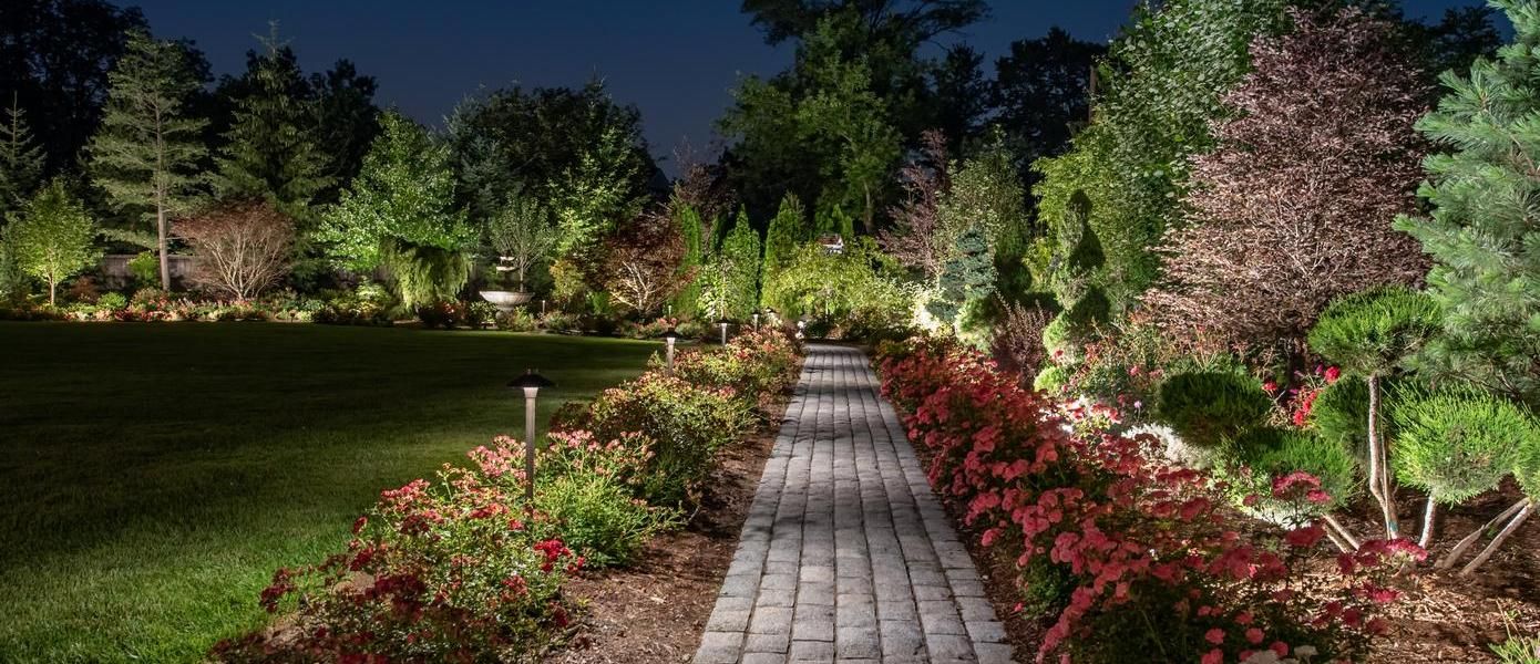 A brick path with flowers and trees at night